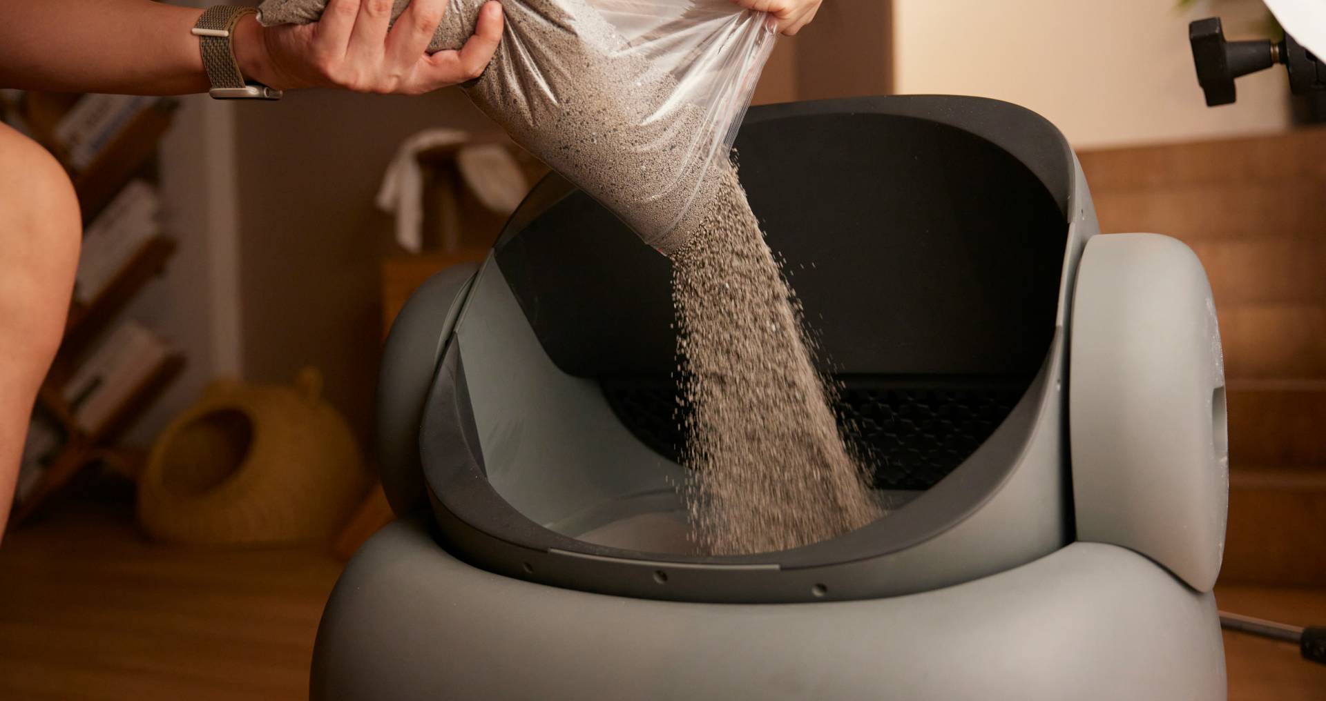Persoon die kattenbakvulling in een open kattenbak giet